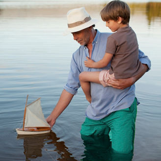 Grandfather and grandson wading in lake with toy sailboat