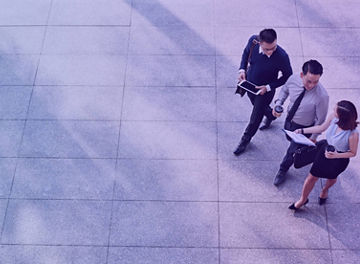 Three business professionals walking together on a large tiled floor, holding documents and a tablet.