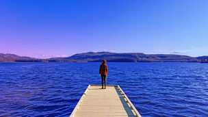 Fotografía de una mujer parada al borde de un muelle mientras observa el horizonte