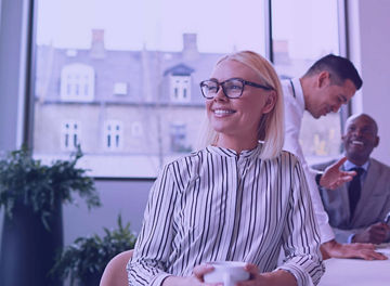 Mulher sentada a conversar com colegas num escritório iluminado.