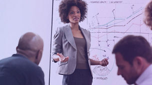 Team meeting with a woman presenting next to a screen.