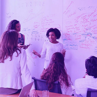 Group of colleagues discussing ideas in a meeting room with a board behind them covered in written notes