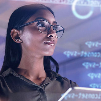 Mulher jovem com óculos e tablet na mão, a olhar para cima de forma reflexiva, rodeada por projeções digitais de código informático e dados tecnológicos.