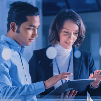 Two professionals, a man and a woman, reviewing information on a tablet in a modern office setting with blue lighting.