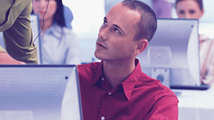 Homem a ouvir instruções de um colega enquanto trabalha num computador.