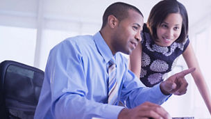 Two professionals reviewing information on a computer monitor in an office.