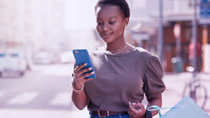 A woman using a cell phone on the street, carrying shopping bags.