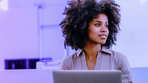 A woman deep in thought in front of a laptop in an office.