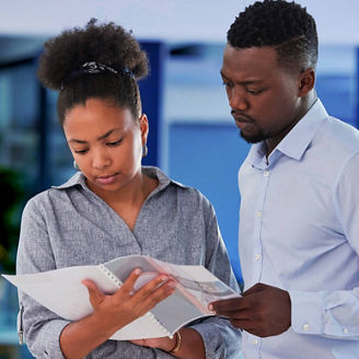 Two professionals, a man and a woman, reviewing information on a tablet in a modern office setting with blue lighting.