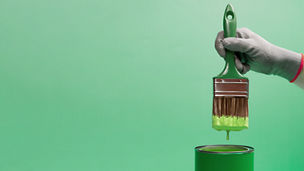 Ein Pinsel der in einen Eimer mit grüner Farbe taucht