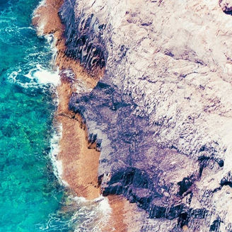 Birds-eye-view of clear blue sea meeting cliffs