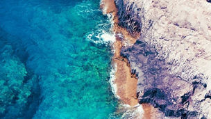 Birds-eye-view of clear blue sea meeting cliffs