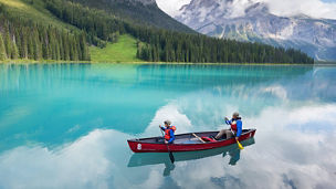 Two people rowing a small wooden boat on a calm river.