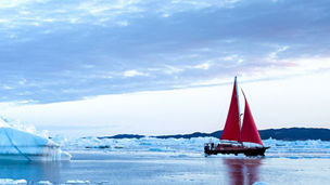 Red sailboat sailing through icebergs