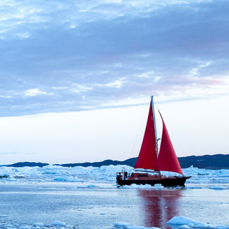 Red sailboat sailing through icebergs
