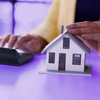 A woman is typing something on a calculator and holding her hand above a miniature house