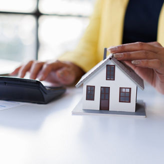 A woman is typing something on a calculator and holding her hand above a miniature house