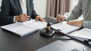 Twee mensen schrijven iets neer op paper en naast hen ligt een rechtershamer.