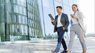 Un homme et une femme marchant devant un batiment d'une entreprise scrollant des smartphones