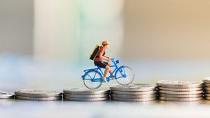 Foto waarin een mannelijk figuurtje een berg van munten opfietst