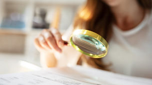 Close-up of a woman holding a magnifying glass above a paper.