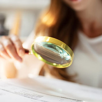 Close-up of a woman holding a magnifying glass above a paper.