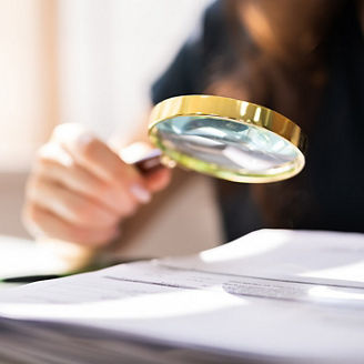 Someone is holding a magnifying glass over papers next to a laptop.