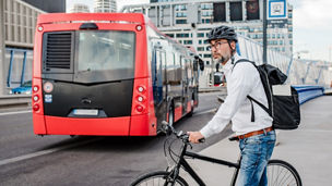 Picture with a road on which a red bus drives and a man is riding a bicycle