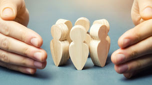 Wooden human-like puppets are surrounded by 2 hands on the side, protecting them.