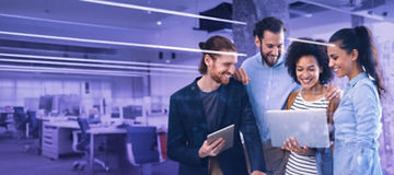 Group of colleagues smiling while looking at a laptop in a modern office environment.