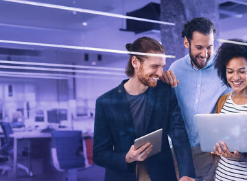 Group of colleagues smiling while looking at a laptop in a modern office environment.