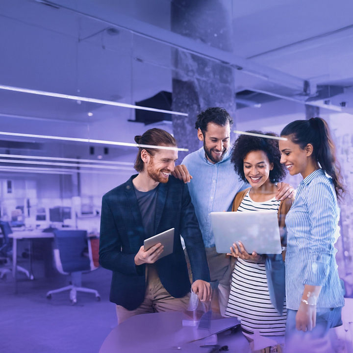 Four young colleagues gathered together discussing ideas while looking at a laptop