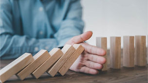 Close-up of a businessman's hands stopping a domino effect