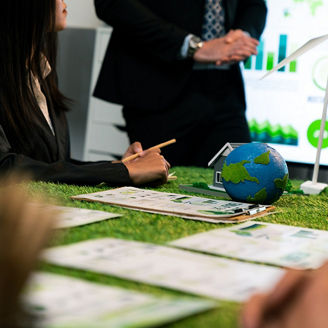 People working around a table with sustainability-related materials, including a small globe, wind turbine model, and documents featuring graphs and charts.