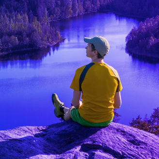 man sitting on the edge of a cliff with a view on a lake