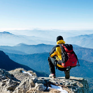 mountineer on cliff looking at mountain range
