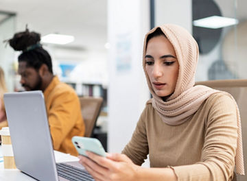 woman wearing hijab, working on her laptop and smartphone