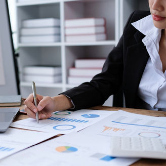 A woman is sitting at her desk with a computer and papers with graphs.