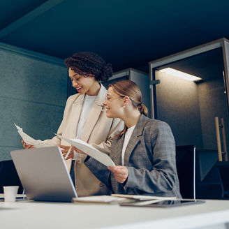 Two smiling business woman work together with documents to get the job done at the office