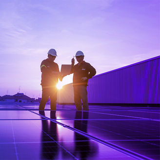 Two construction workers stand near solar panels