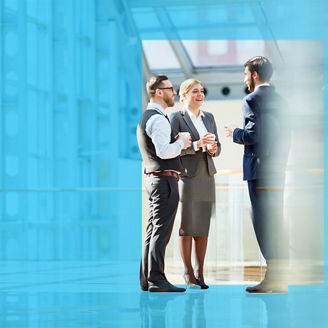 Group of modern business people chatting during coffee break  standing in sunlit glass hall of office building