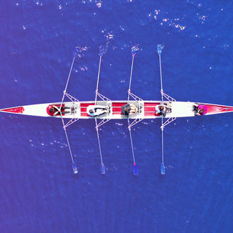 Aerial image of a row boat with 5 people rowing in it.