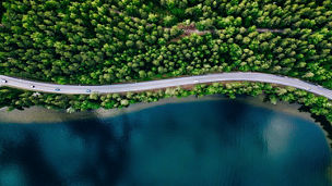 Aerial view of road between green summer forest and blue lake in Finland