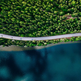 Aerial view of road between green summer forest and blue lake in Finland