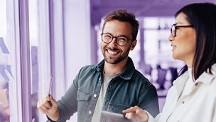 Business man brainstorming with his colleague using sticky notes. Creative business people standing next to a window and discussing their ideas.; Shutterstock ID 2371350991; purchase_order: Advisory assurance; job: anne; client: Future of audit campagne