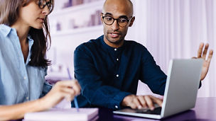 Business man using a laptop and discussing with his colleague in an office. Black business man having a meeting with a female professional.; Shutterstock ID 2363383347; purchase_order: advisory assurance; job: anne; client: ai