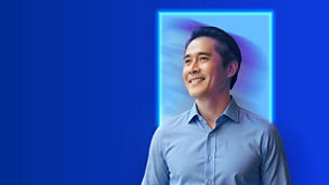Swmiling man in blue shirt standing in front of light blue square
