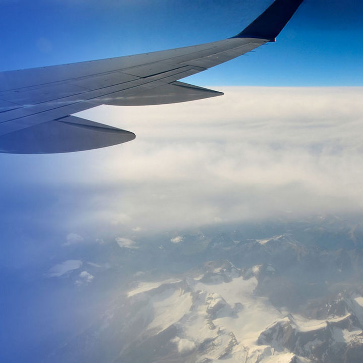 Airplane wing flying over clouds and mountains
