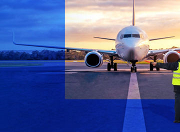 A commercial airplane is positioned on an airport runway with ground operations visible in the foreground.