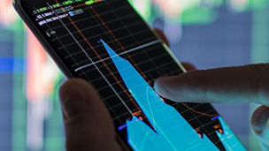A zoomed in shot of a hand holding a smartphone with graphs on the screen